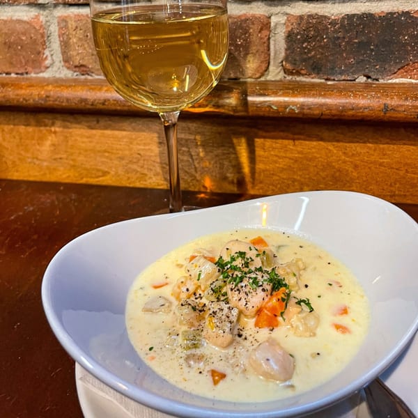 Creamy seafood chowder with vegetables and herbs, next to a glass of white wine.