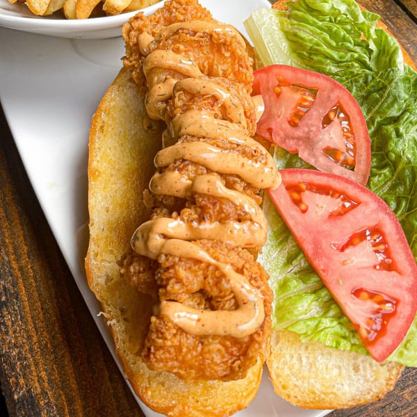 Crispy fried shrimp po'boy with creamy sauce, lettuce, and tomato on a white plate.