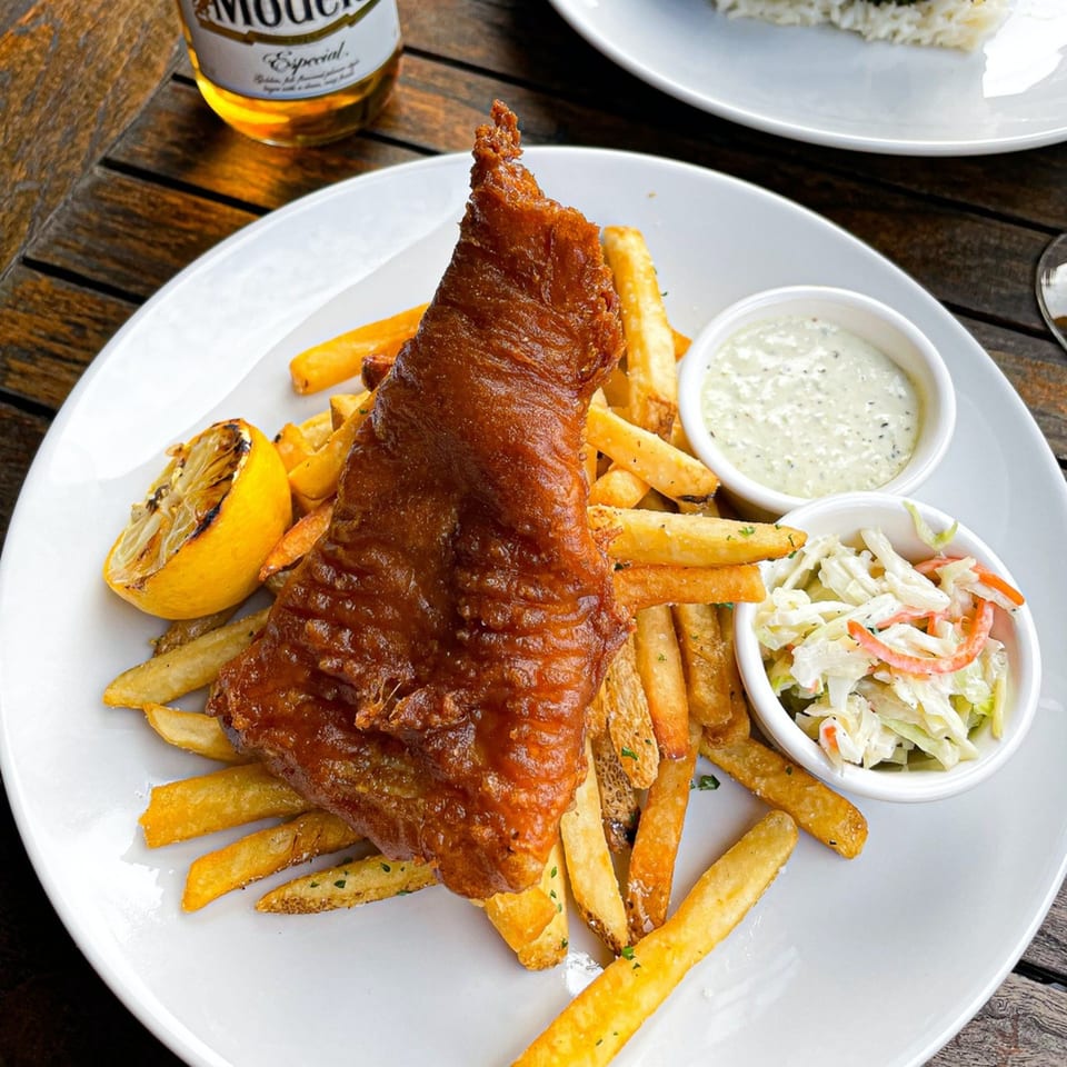 Crispy fish and chips with coleslaw, tartar sauce, and a grilled lemon on a white plate.